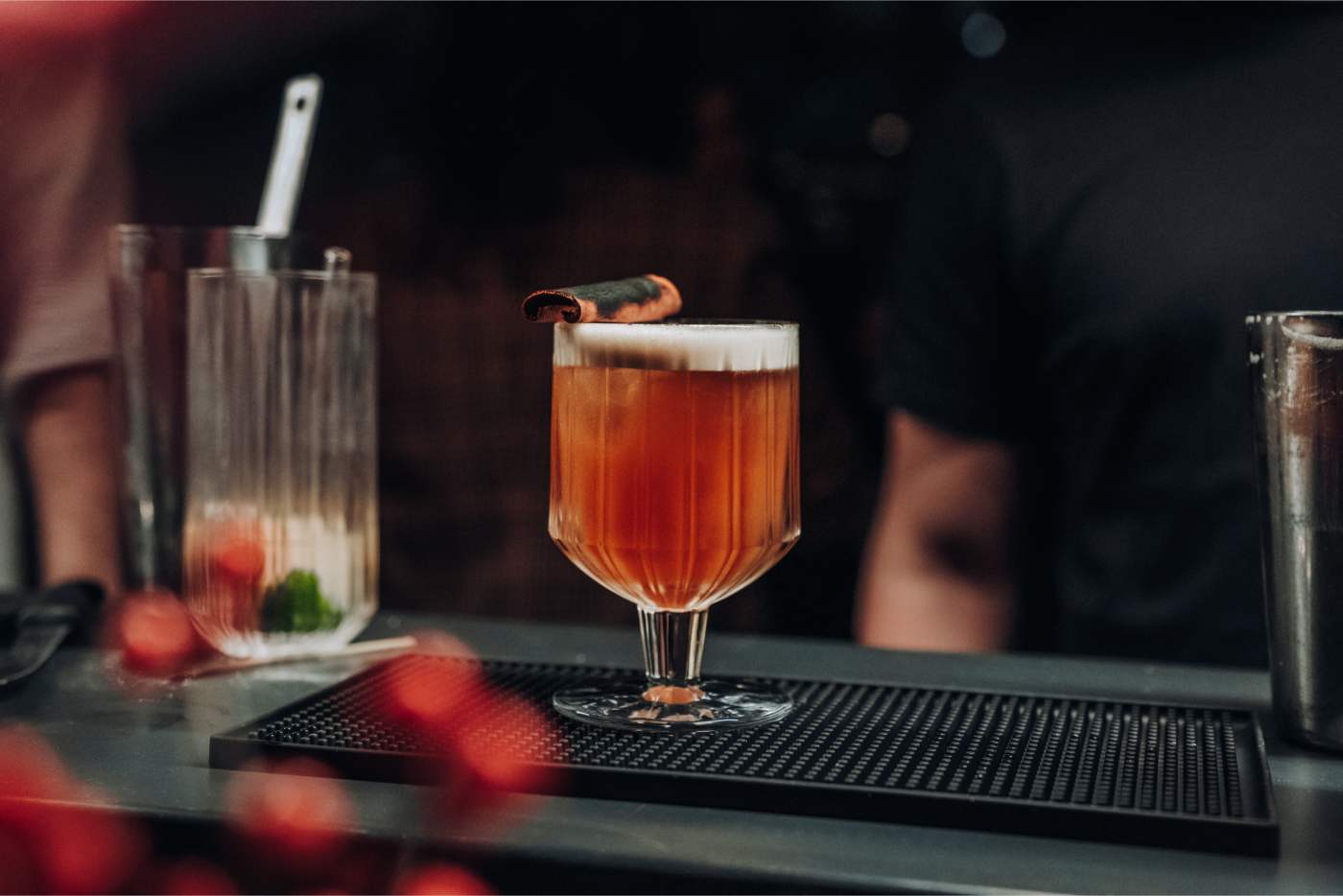 Professioneller Barkeeper mixt orangefarbenen Cocktail mit weißem Schaum und Garnitur auf schwarzer Barmatte