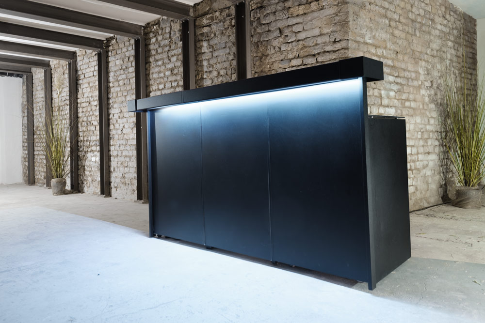 Moderne schwarze mobile Bar mit LED-Beleuchtung in industriellem Loft mit Backsteinwänden und Betonboden