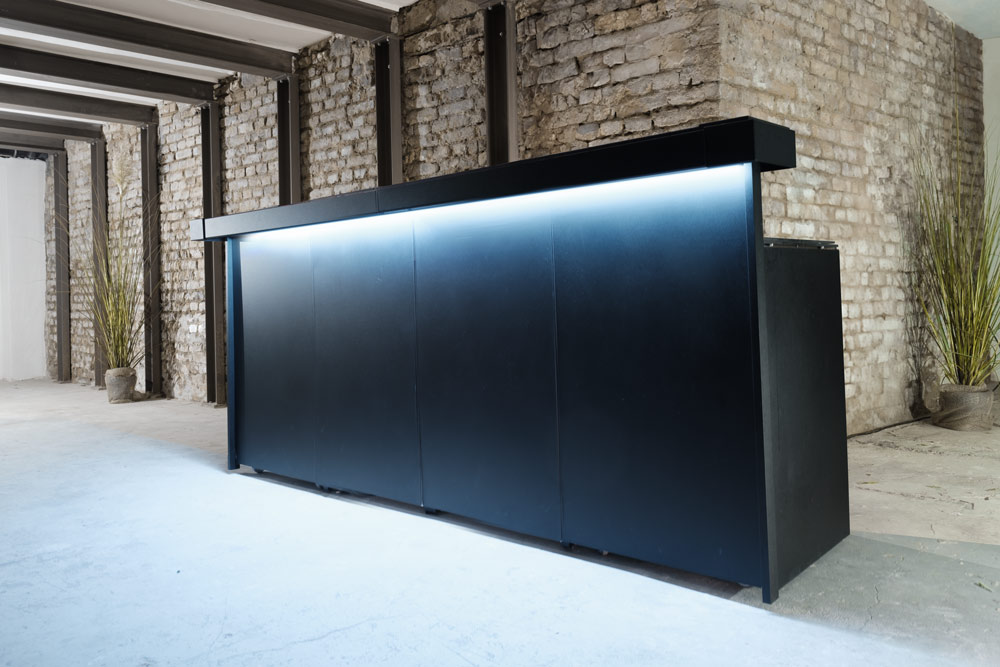 Moderne schwarze mobile Bar mit LED-Beleuchtung in industriellem Loft mit Backsteinwänden und Betonboden