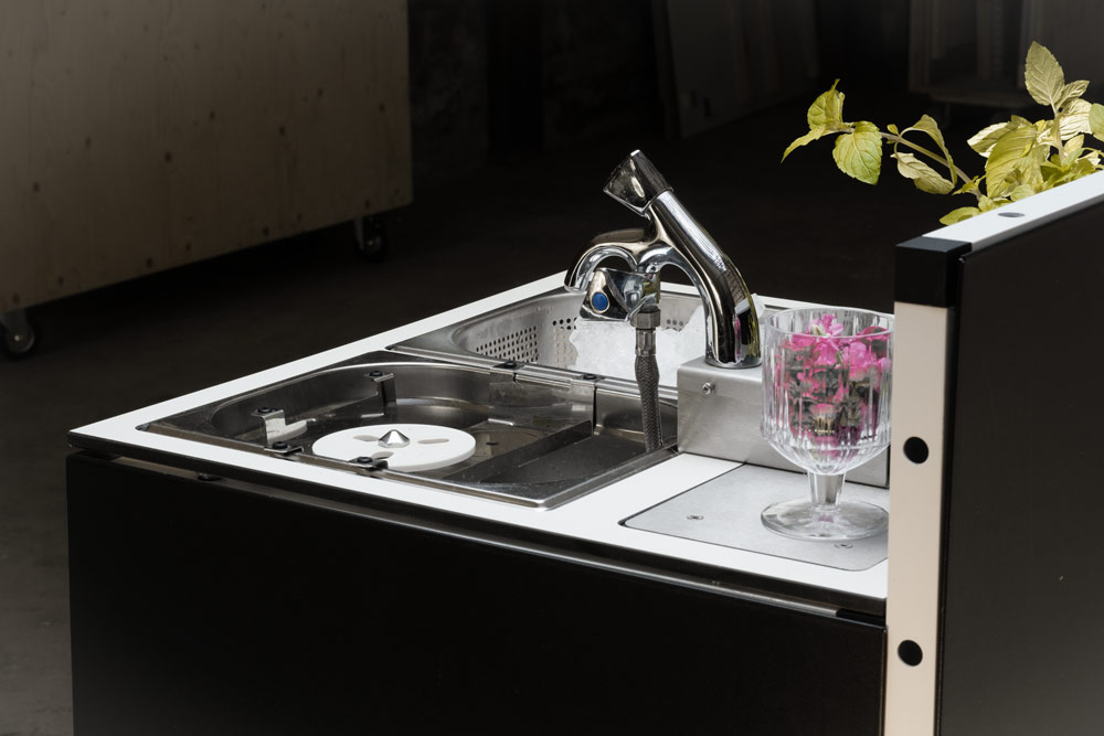 Mobile Cocktailbar mit integriertem Waschbecken, Wasserhahn und dekorativem Glas mit pinken Blumen auf weißer Arbeitsplatte