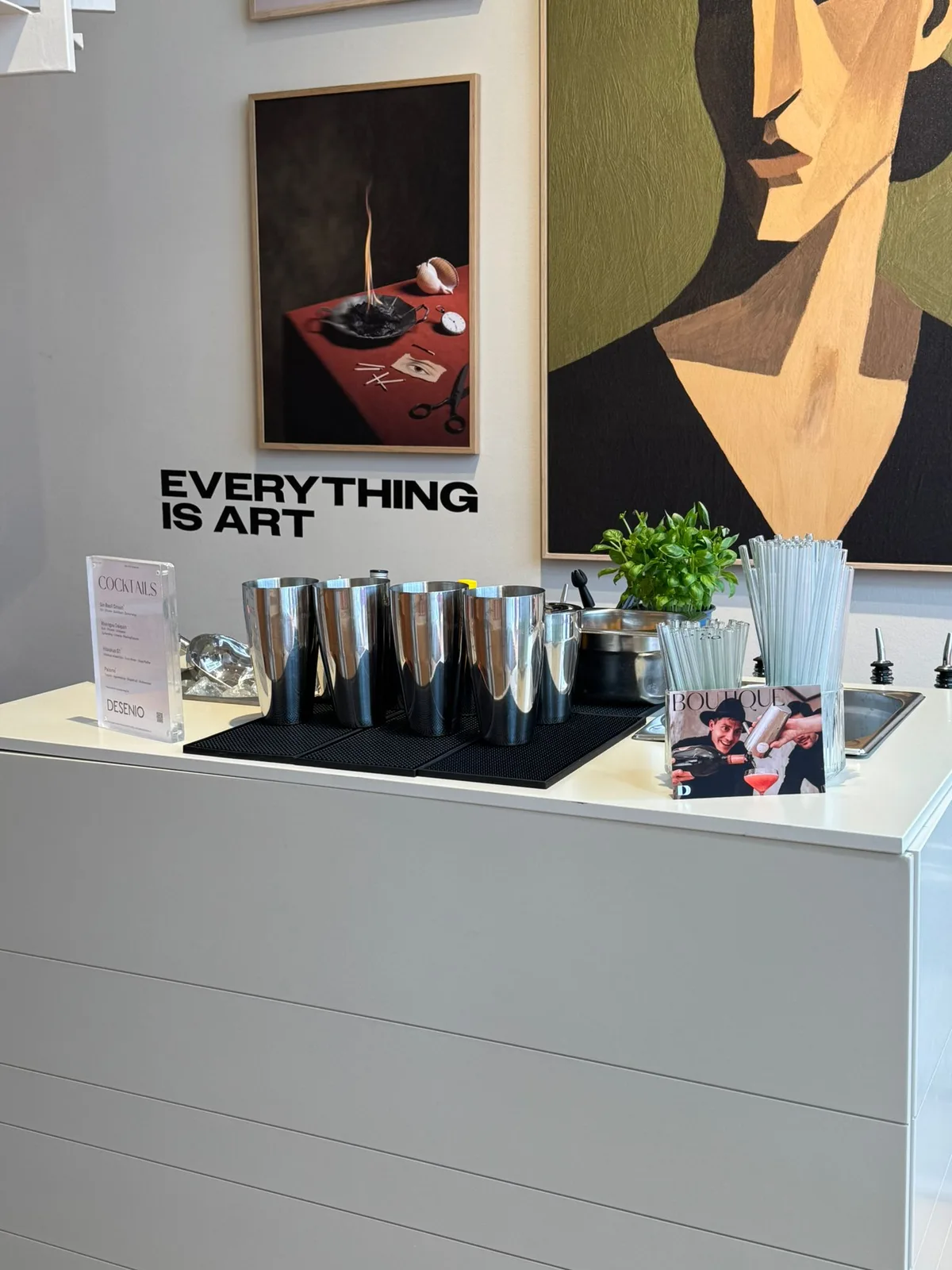Bar-Setup mit Shakern, Cocktailkarte und Basilikum vor dem Schriftzug Everything is Art