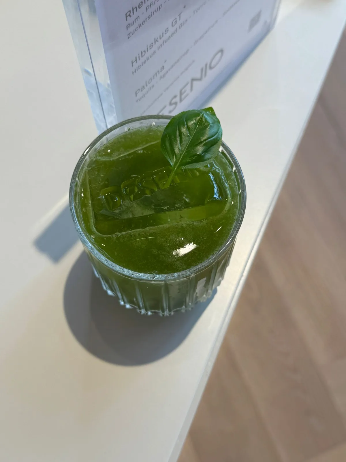 Basilikumgrüner Signature-Cocktail mit Desenio-Eiswürfel auf der gebrandeten Bar in Köln
