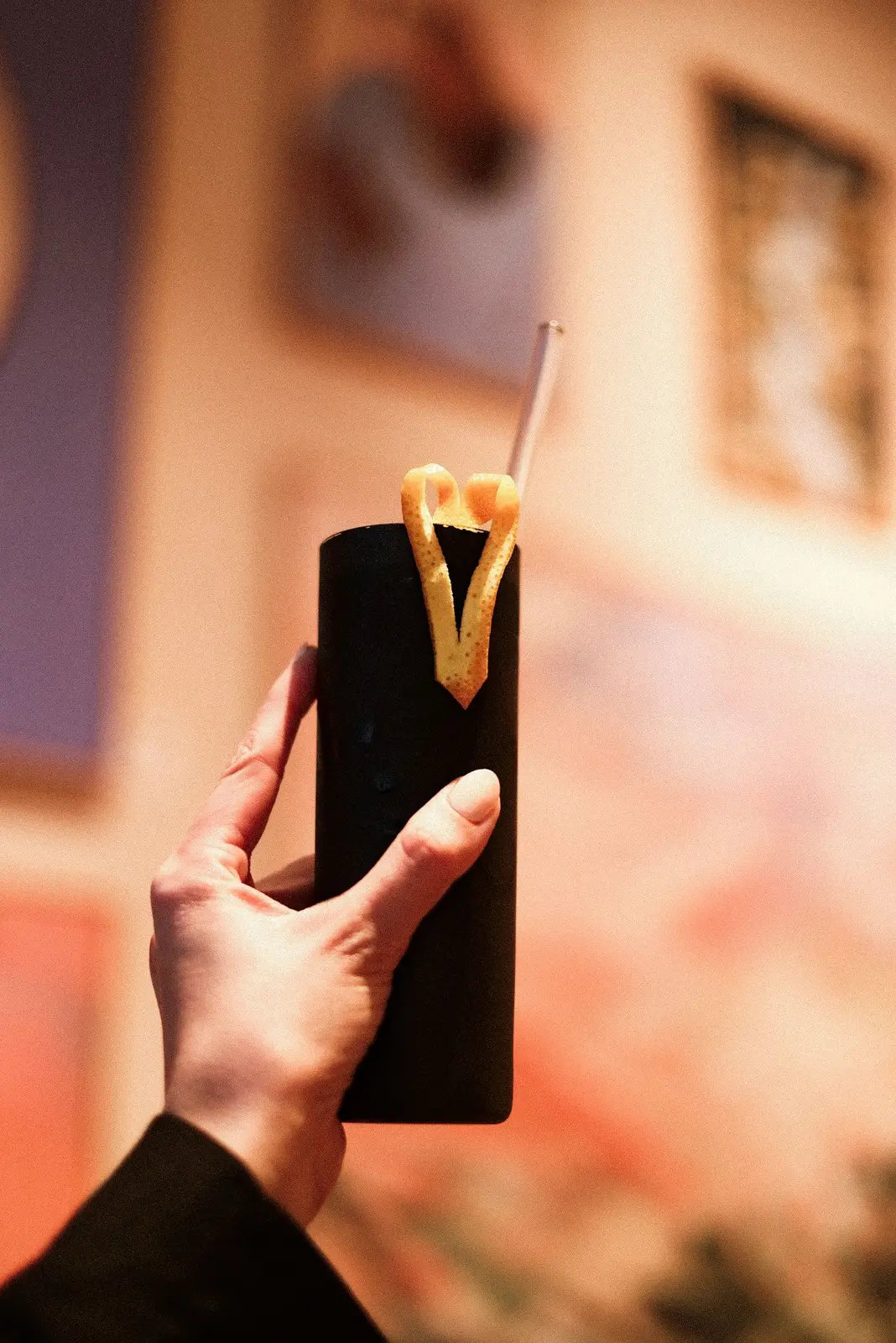 Signature-Drink im matt-schwarzen Becher mit Orangenzesten-Garnitur und Glasstrohhalm