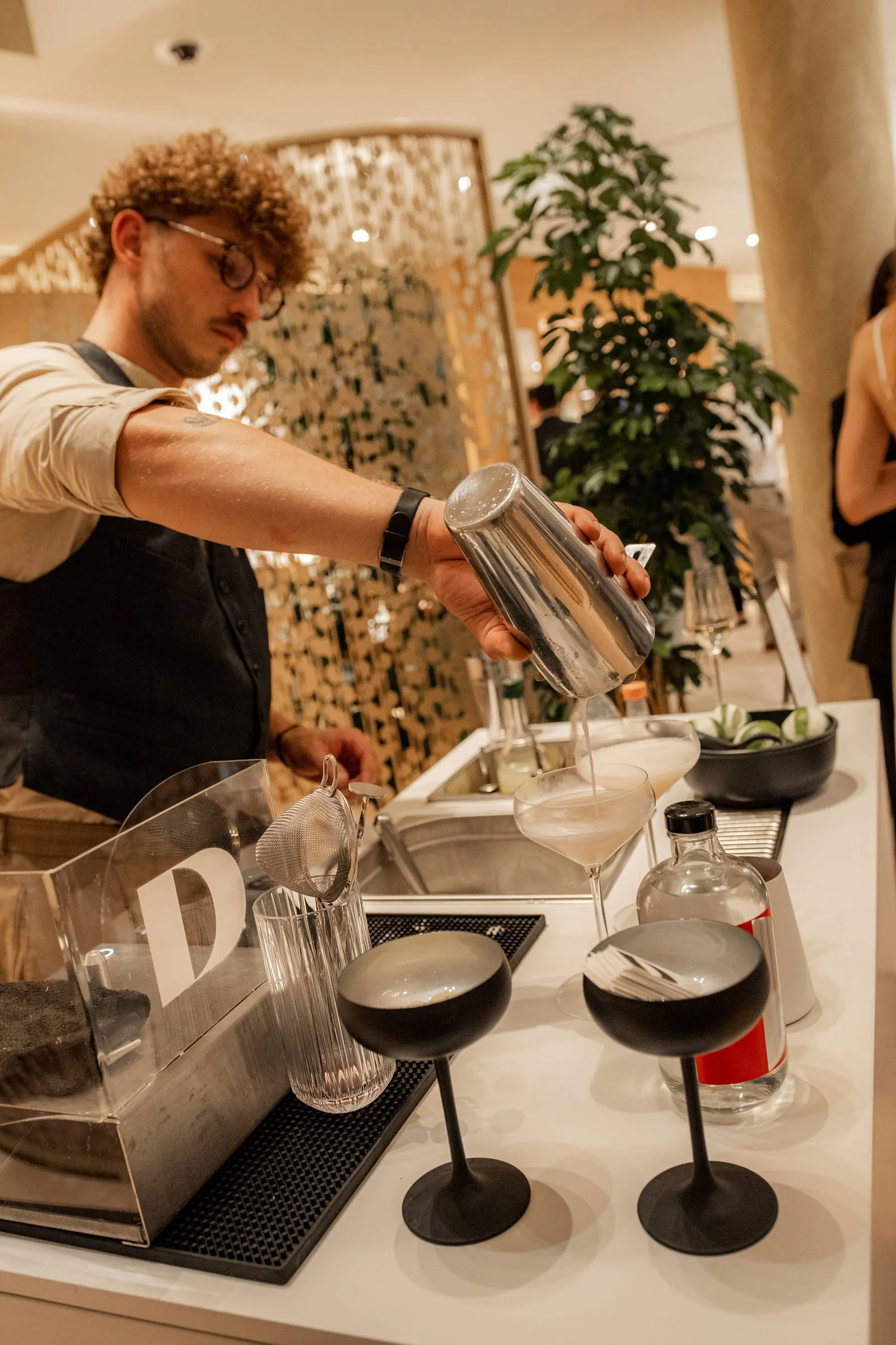 Hinter einer Acrylscheibe mit gelasertem Logo gießt der Barkeeper an der mobilen Bar in Wien in Coupettes