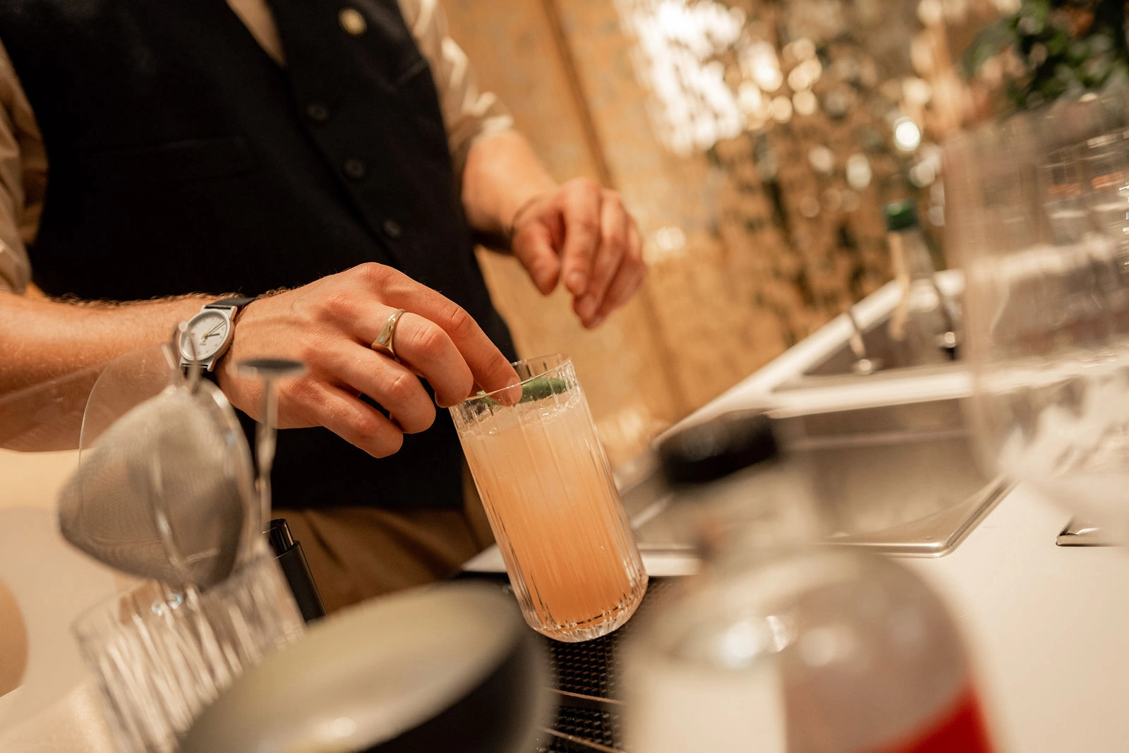 Ein heller Cocktail im hohen Glas wird beim Cocktailservice in Wien garniert, davor unscharfes Werkzeug