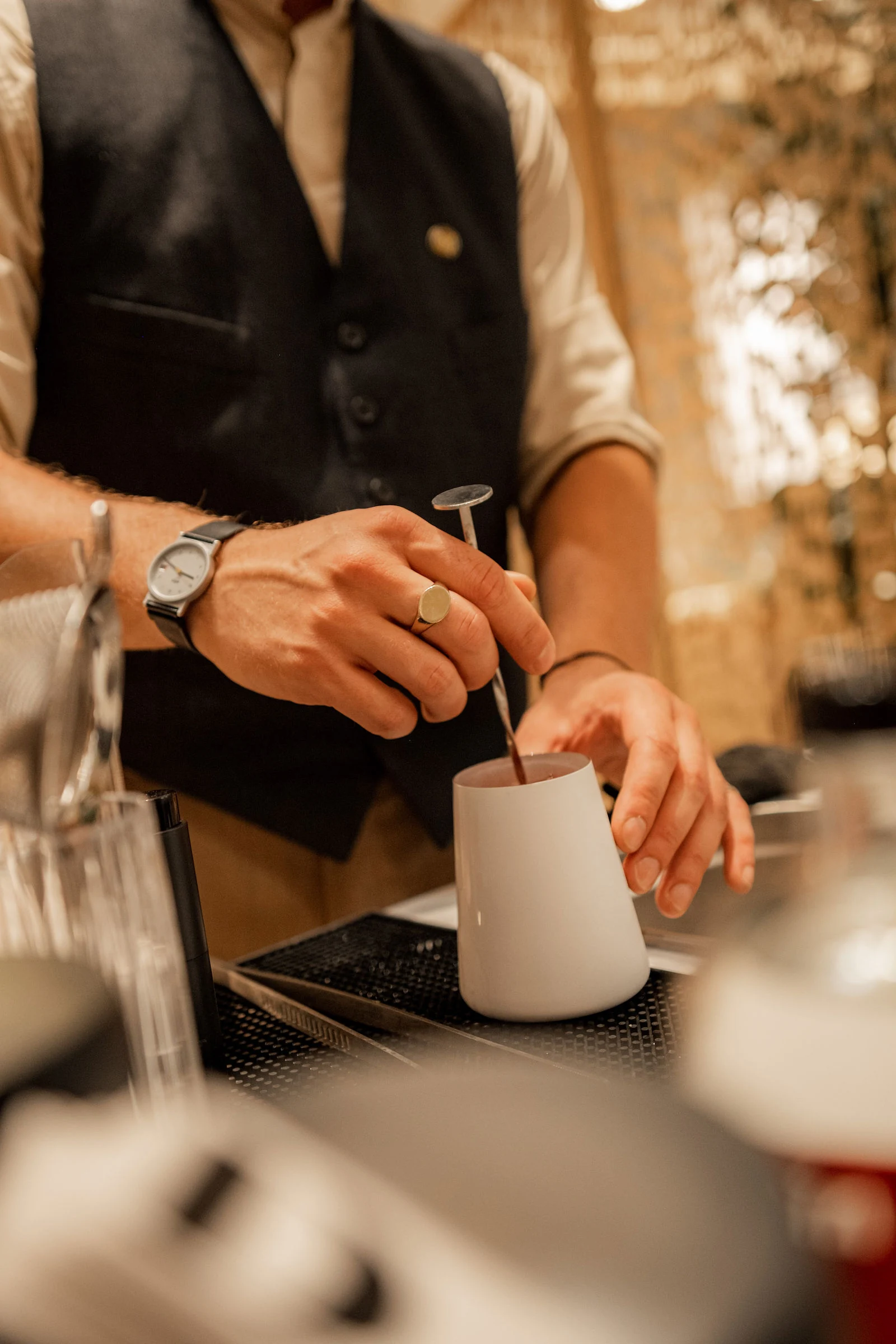 Hände beim Rühren im weißen Rührbecher, daneben liegt Barwerkzeug auf der mobilen Theke in Wien