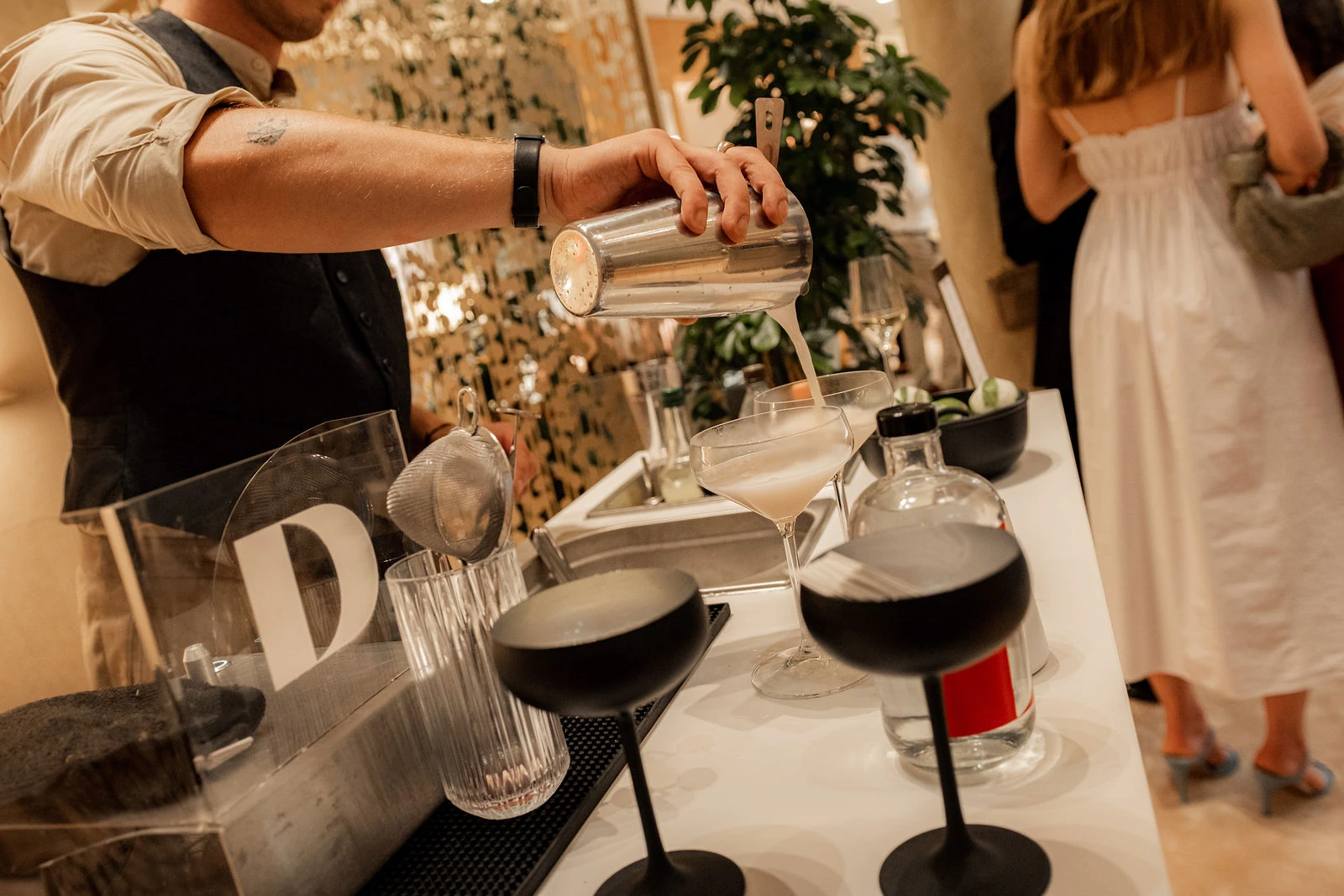 Cocktail fließt in zwei Coupette-Gläser, davor steht eine Acrylscheibe mit gelasertem Logo beim Event in Wien