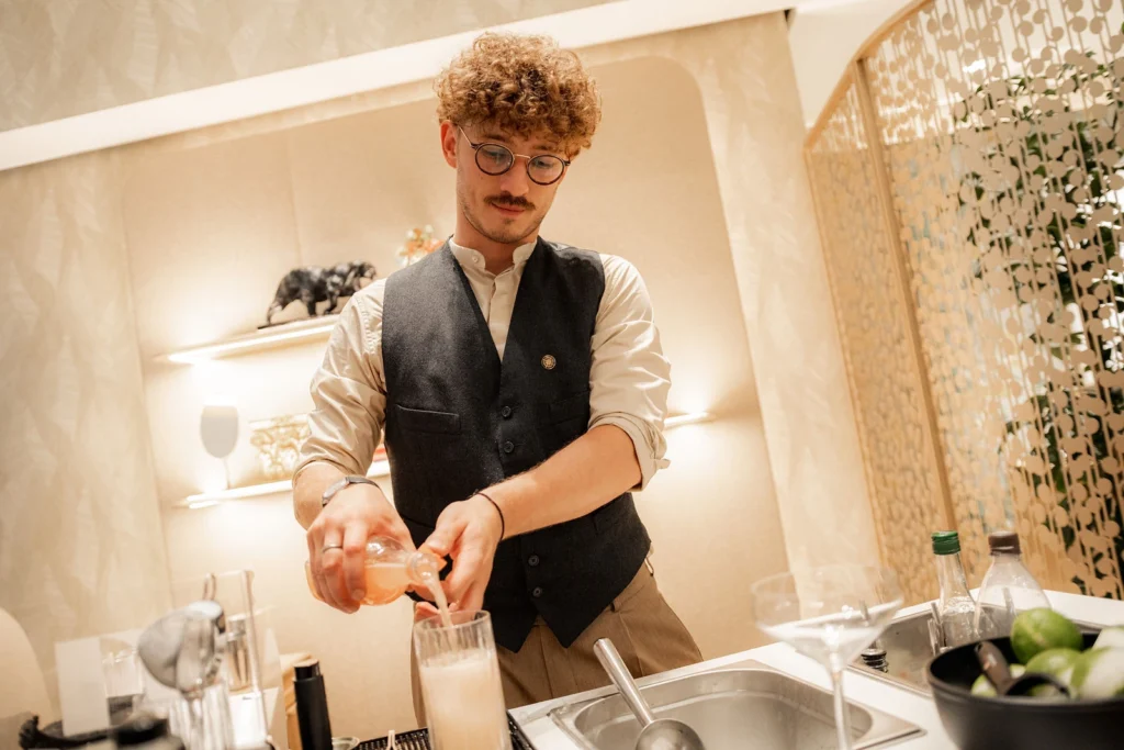 Barkeeper in Wien beim Abseihen eines Cocktails durch ein Barsieb an der weißen mobilen Theke