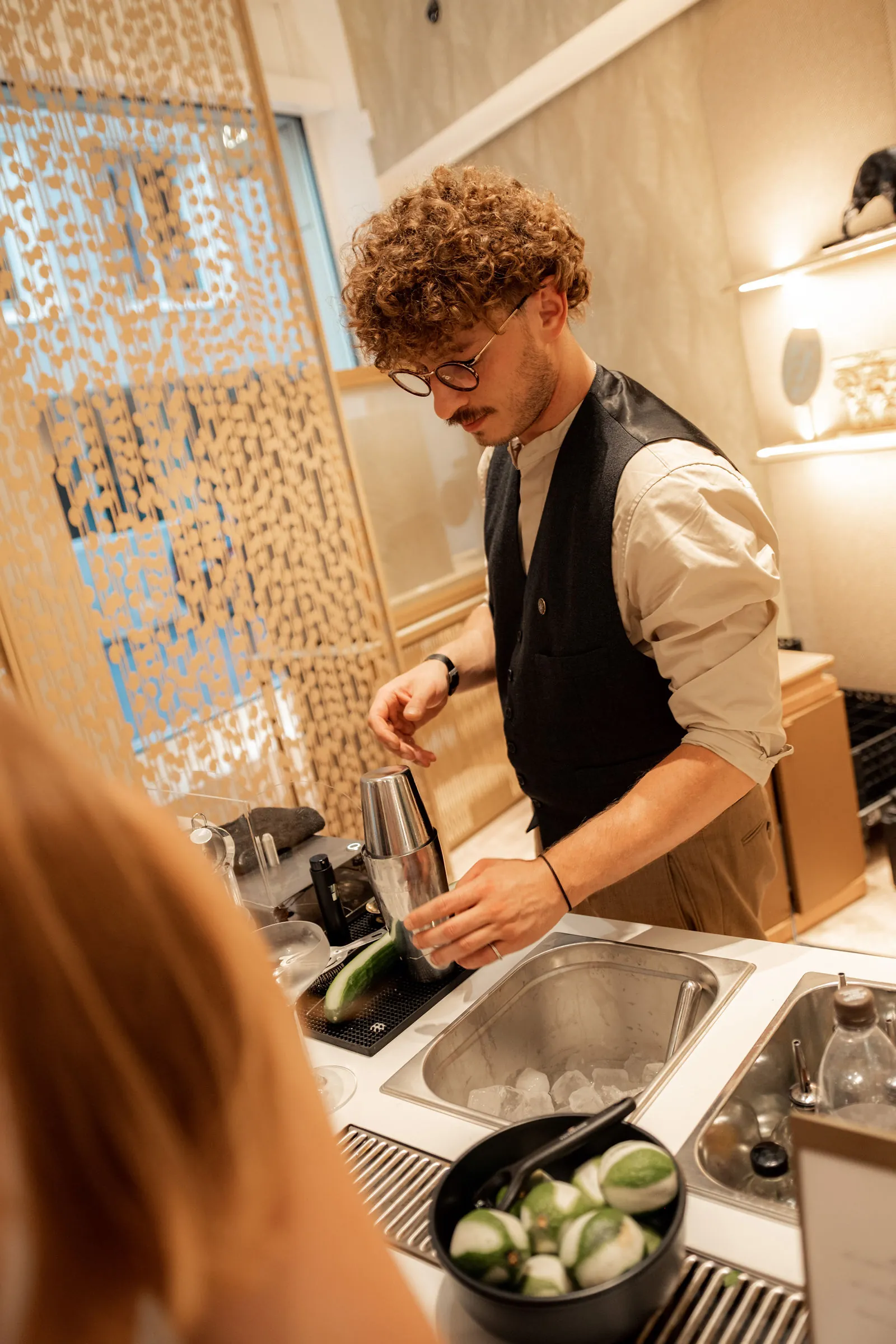 Am Eisfach arbeitet unser Bartender in Wien, auf der weißen Theke stehen Gläser neben Limetten