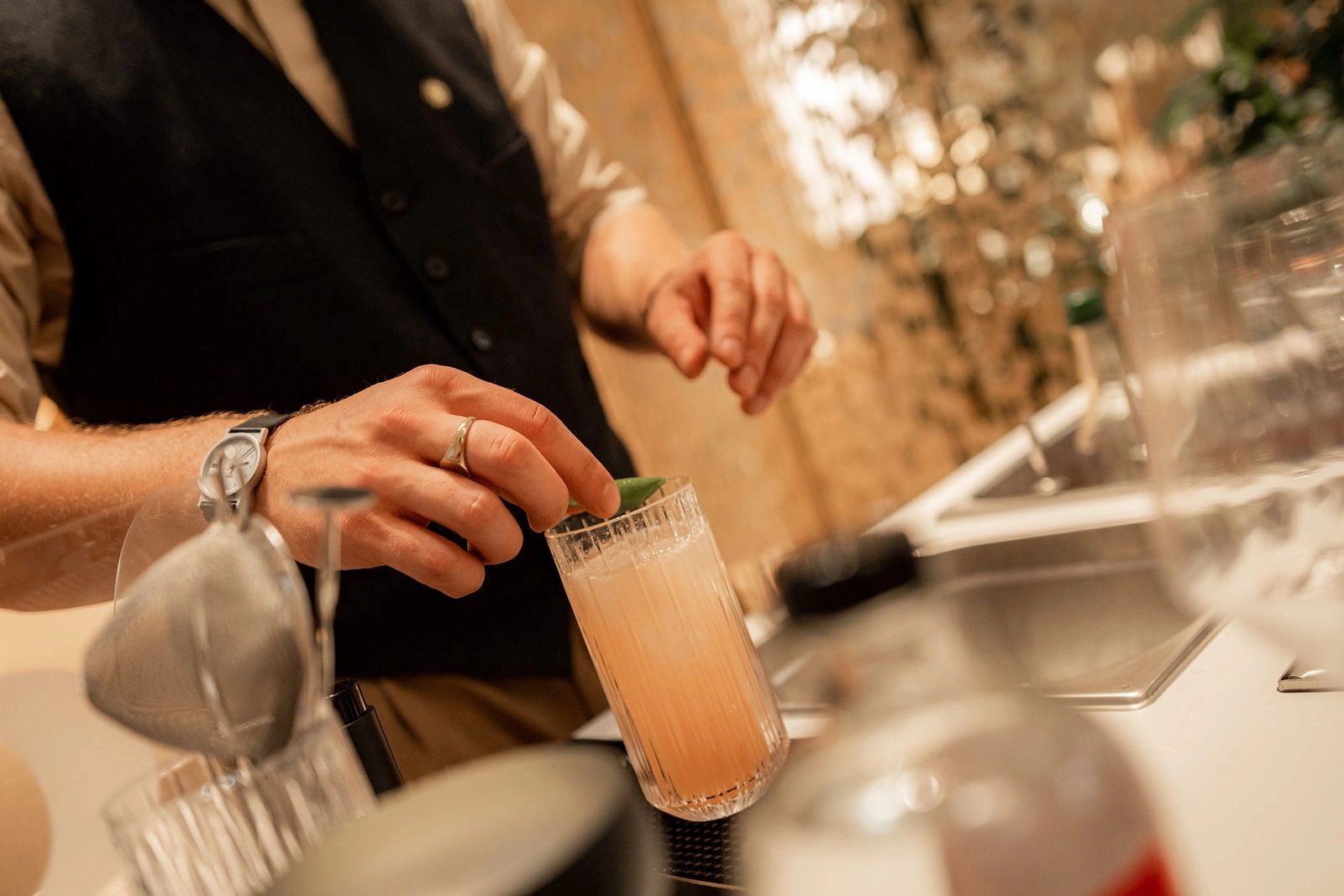 Hände setzen beim Cocktail Catering in Wien eine Kräutergarnitur auf einen hellen Drink im hohen Glas